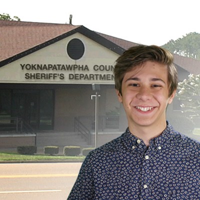 Smiling teen boy with medium brown hair with the sheriff's department in the background
